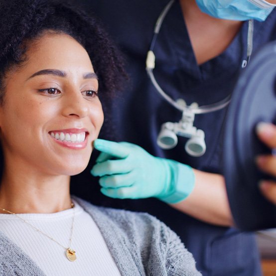 Woman smiling in the mirror after learning the cost of cosmetic dentistry in Jupiter