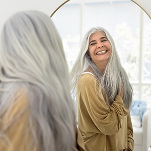 Older dental implants patient in Jupiter smiling in the mirror