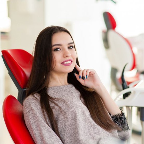 Woman smiling in patient’s chair and tapping her chin