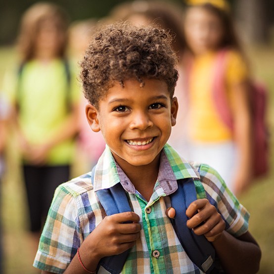 Small boy wearing a backpack at school and smiling