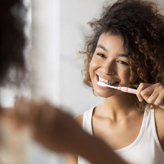 Woman smiling as she brushes her teeth in mirror