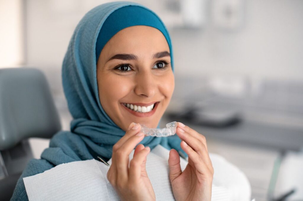 A woman at the dentist putting on an Invisalign aligner.