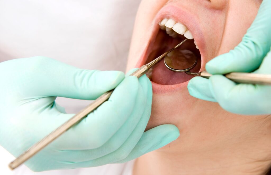 Green-gloved hands holding dental instruments to examine patient's mouth