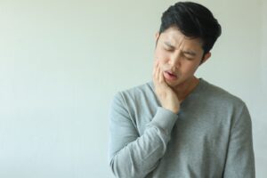 Man with head tilted to side holding jaw in pain.
